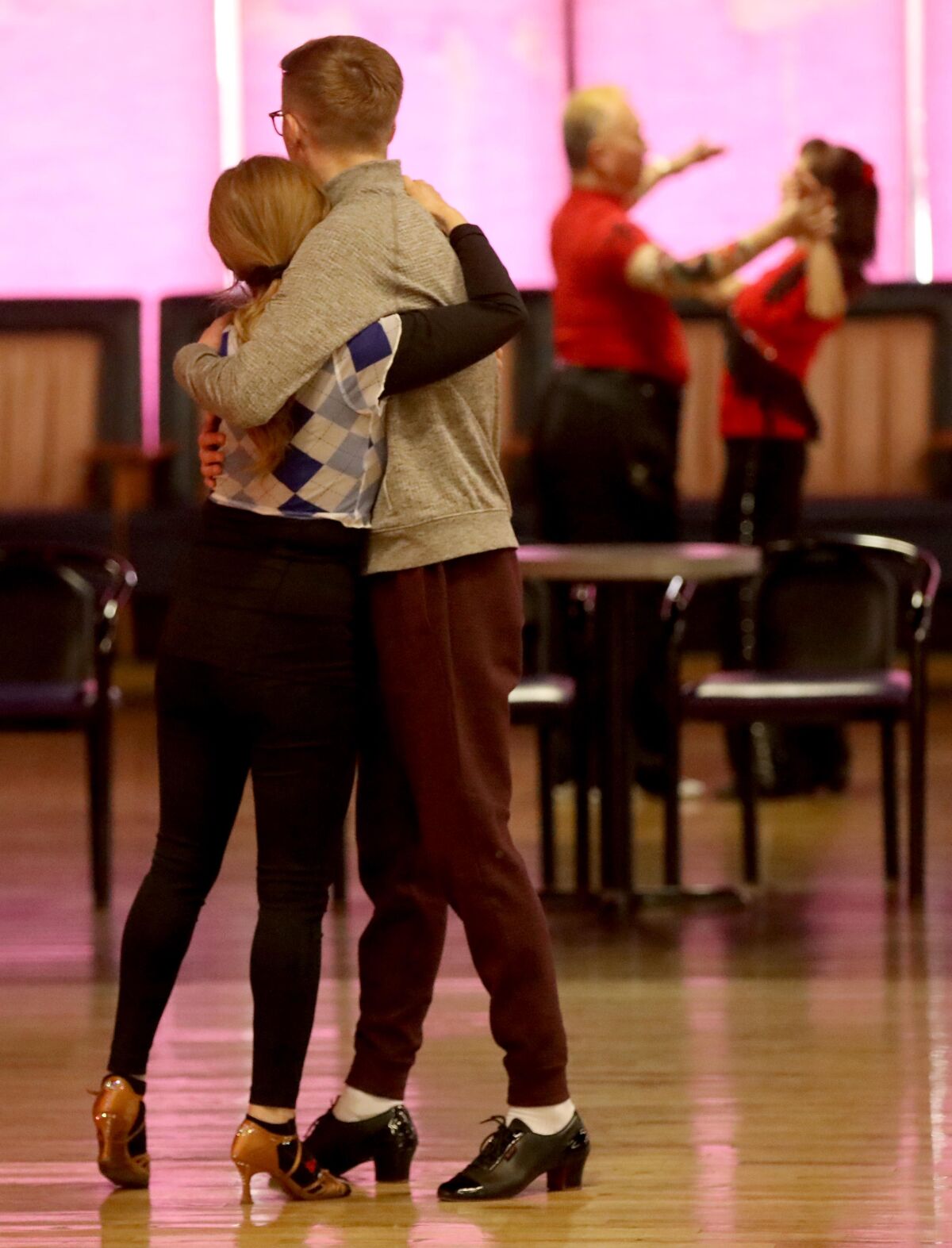 A woman in low heels and a man in dance shoes embrace on a dance floor.