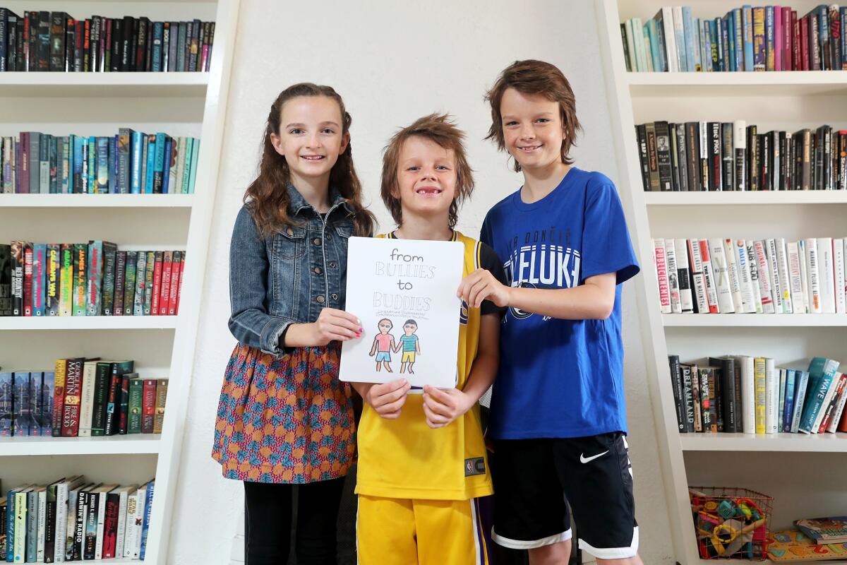 Troutman children, twins Meka, left, and Dirk, right, both 11, with younger brother Beck, 7, show off their book.