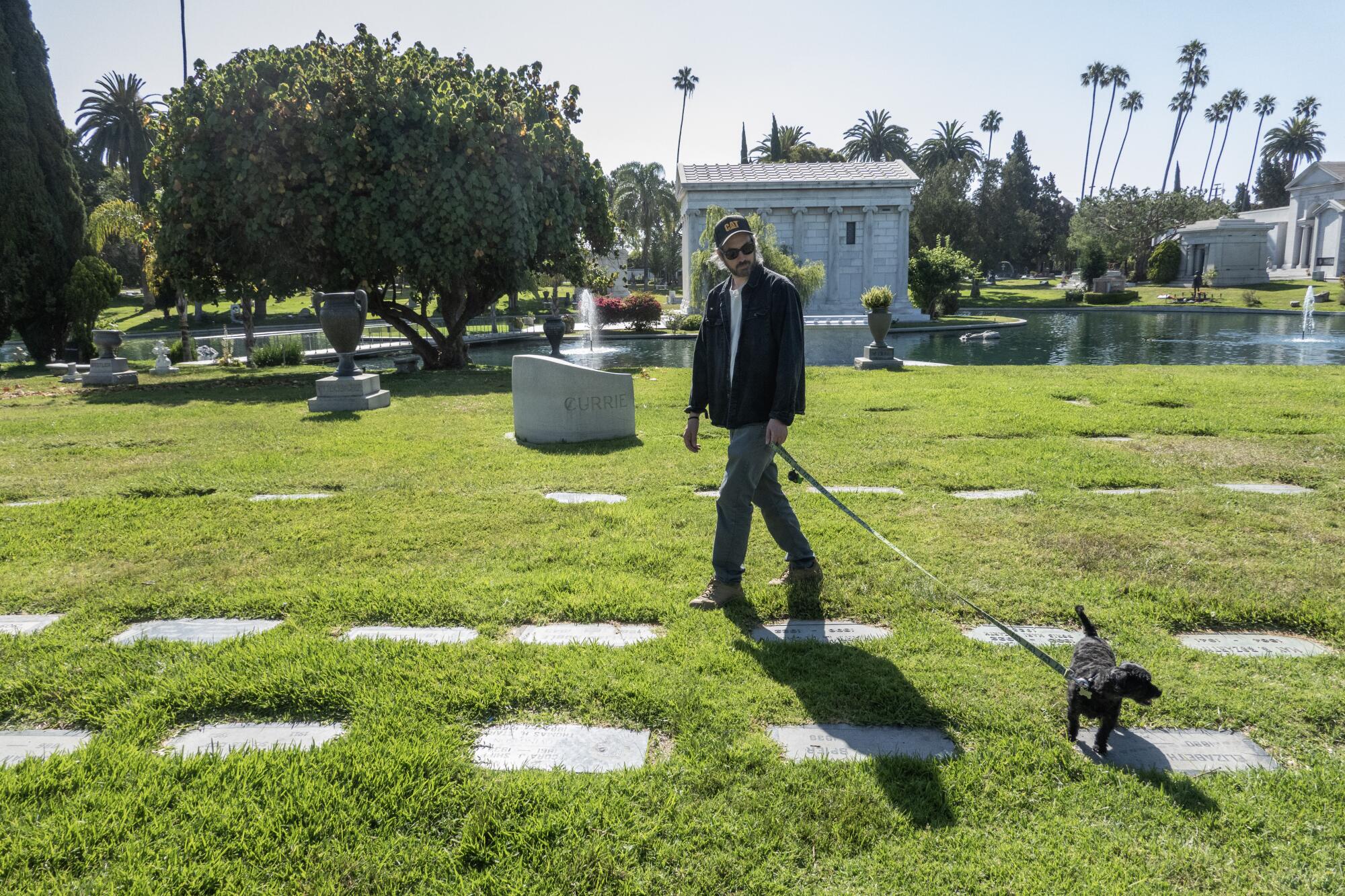 A man and his black dog walk in a Los Angeles cemetery.