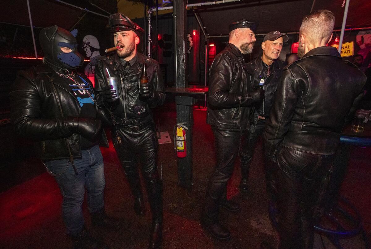 Charlie Wittke, second from left, enjoys a cigar alongside "Pup Too," on a leash, at the SF Eagle in San Francisco's Leather and LGBTQ Cultural District.