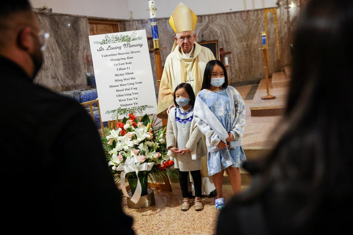 Two young girls stand with a Catholic archbishop in clergy robes 