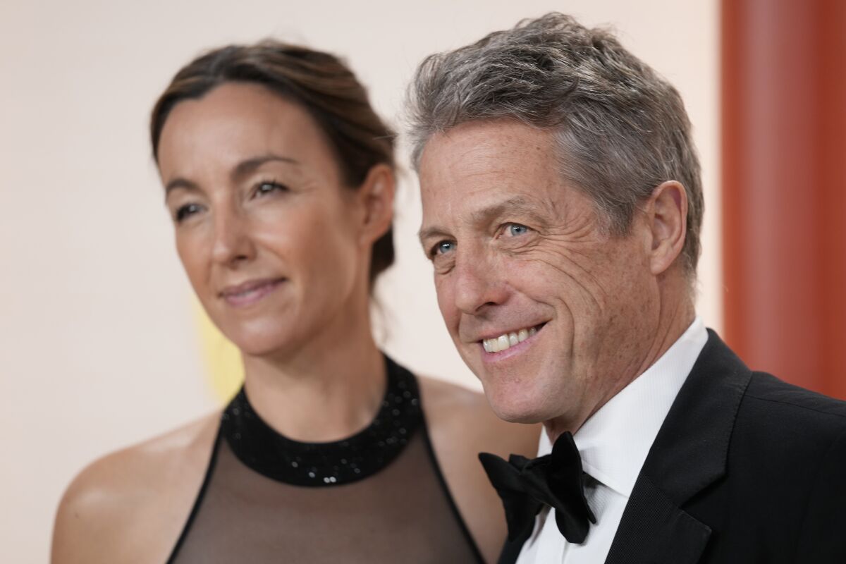 Actor Hugh Gramt in a tuxedo standing next to a woman in a sheer black dress