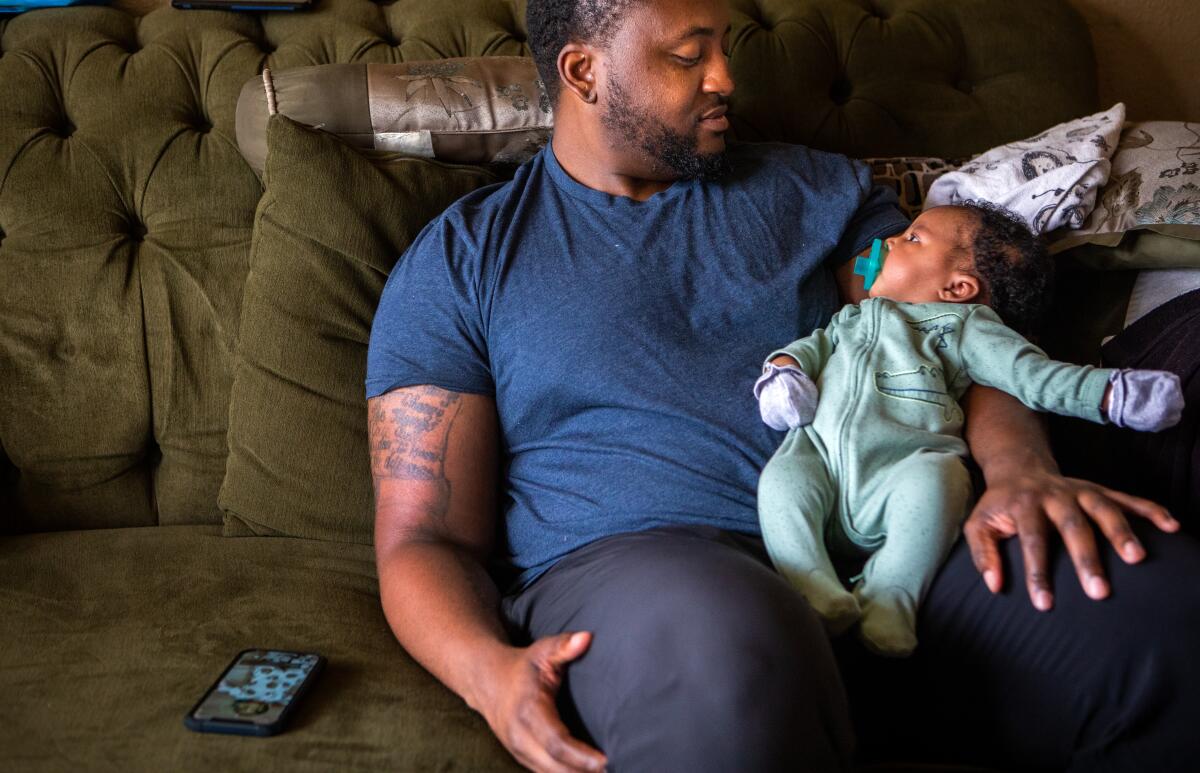 A father sitting on a couch holds his newborn baby boy.