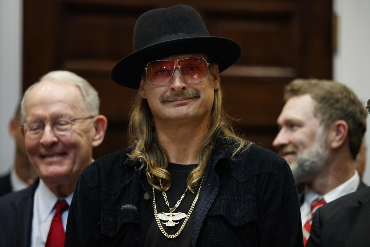 Kid Rock smirks while at the White House in a black hat, black outfit, gold chains and tinted shades 