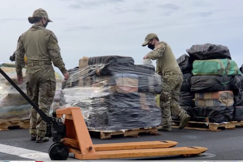 U.S. Coast Guard and U.S. Navy personnel offload pallets of bagged drugs.