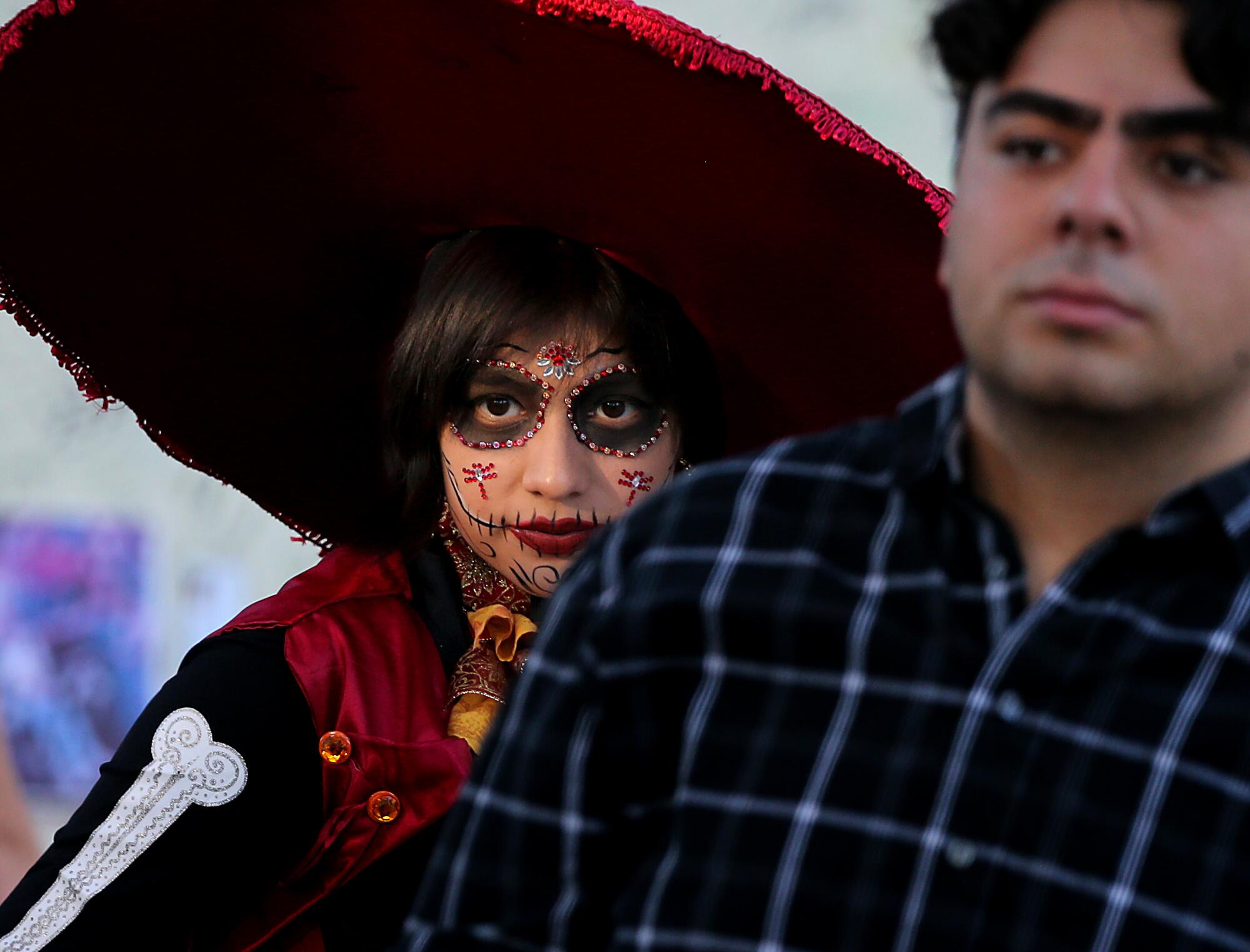 Meztly Villegas wears a red catrina dress and face paint while standing near a man.