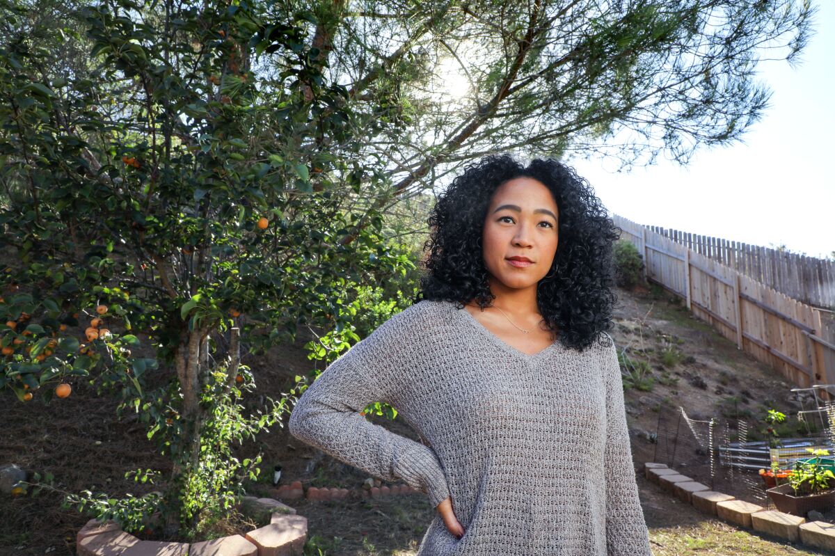 Beverly Johnson shown from the waist up, in front of a fruit tree and wearing a grey sweater 