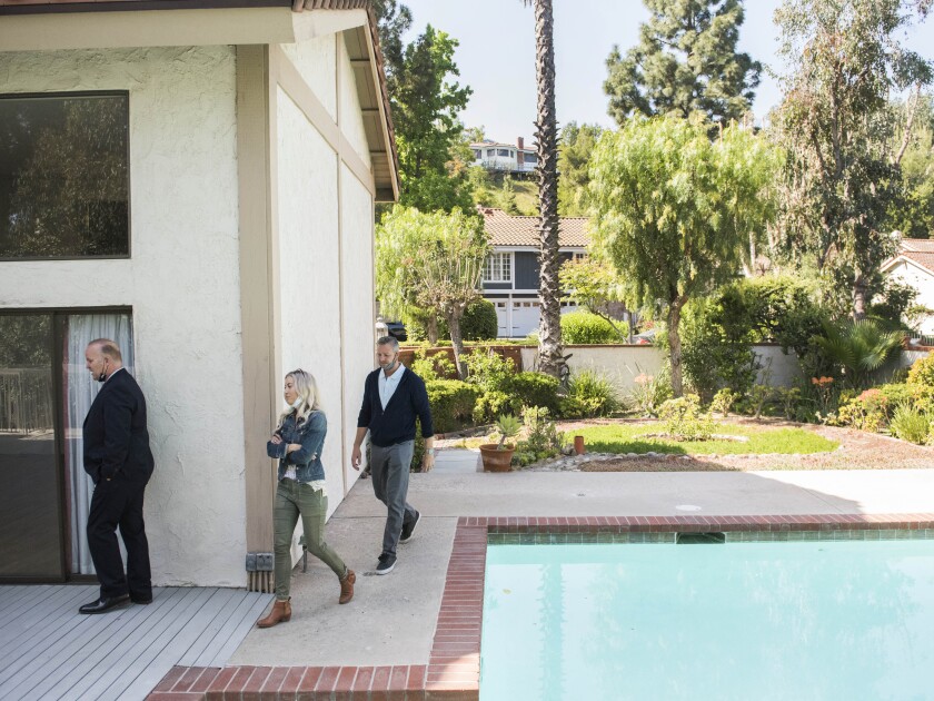 Three people walk past a swimming pool as they tour a California home for sale.