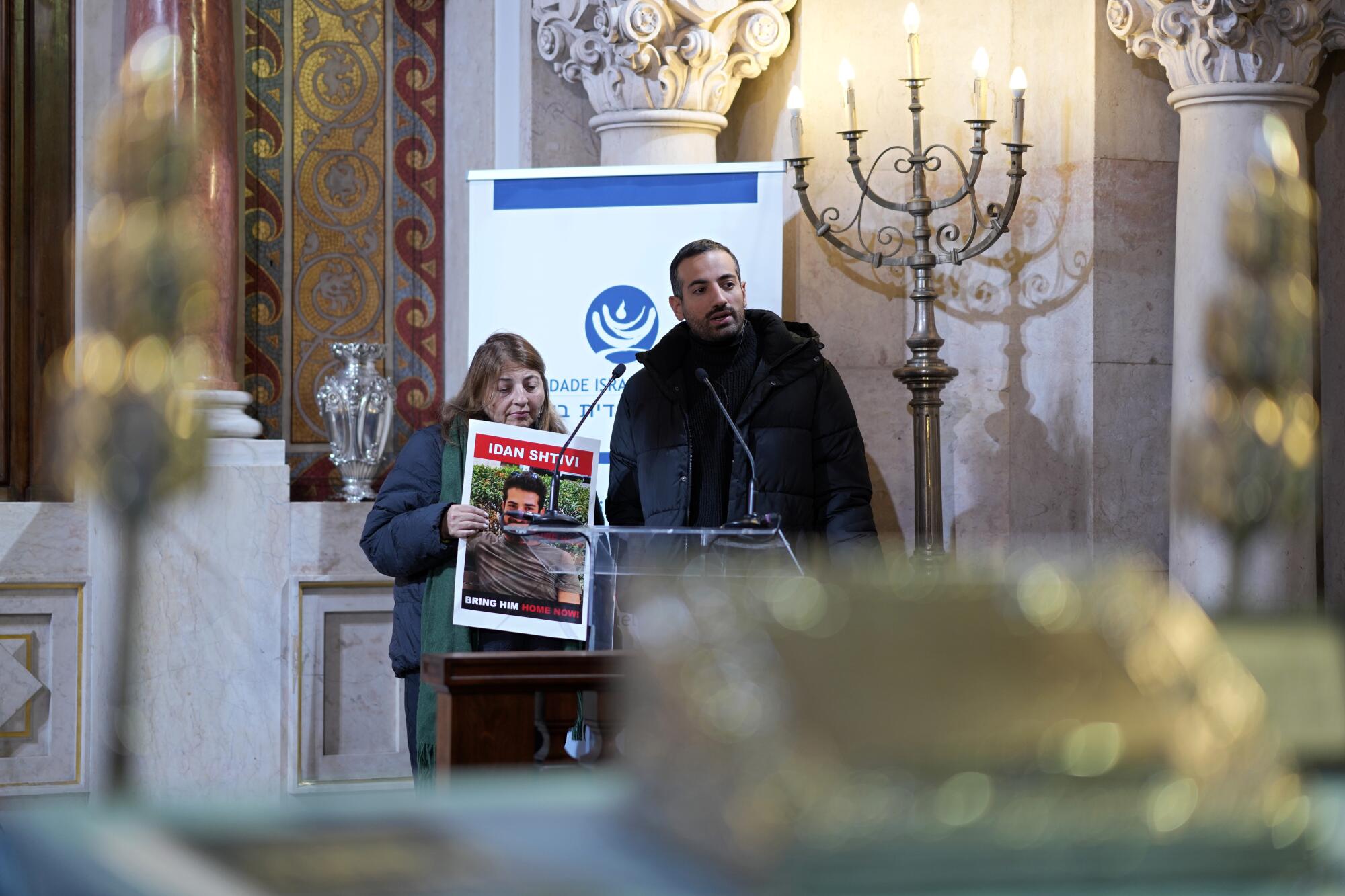 Two siblings of an Israeli hostage in Gaza holding up his photo in a synagogue.