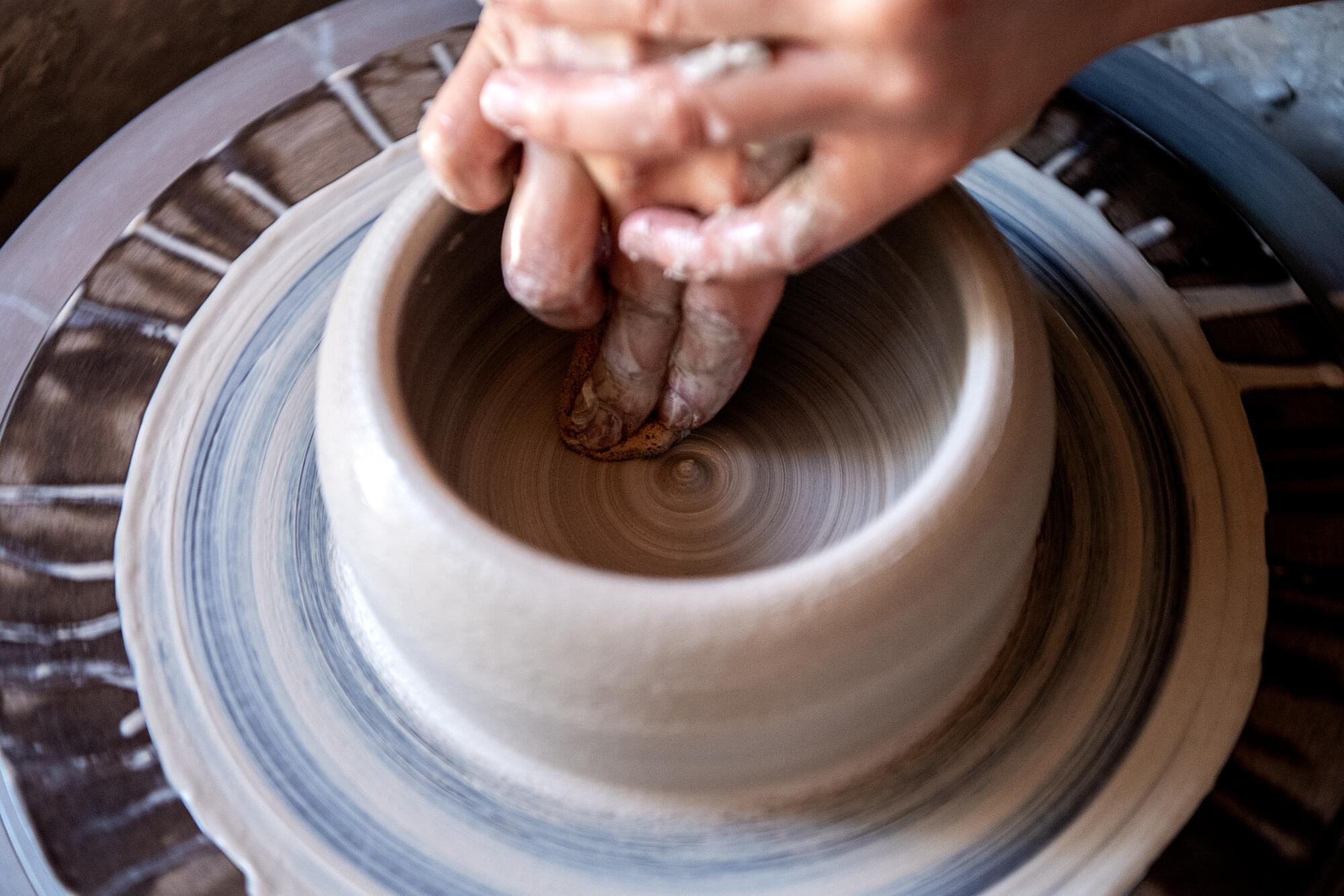 A close-up on a woman's hands as she shapes clay on a wheel.