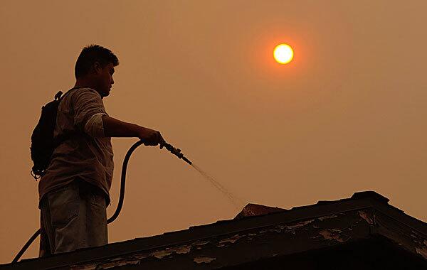 Josh Yeh, whose family chose to ignore a mandatory evacuation order, uses a garden hose to keep his roof wet in La Ca?ada Flintridge.