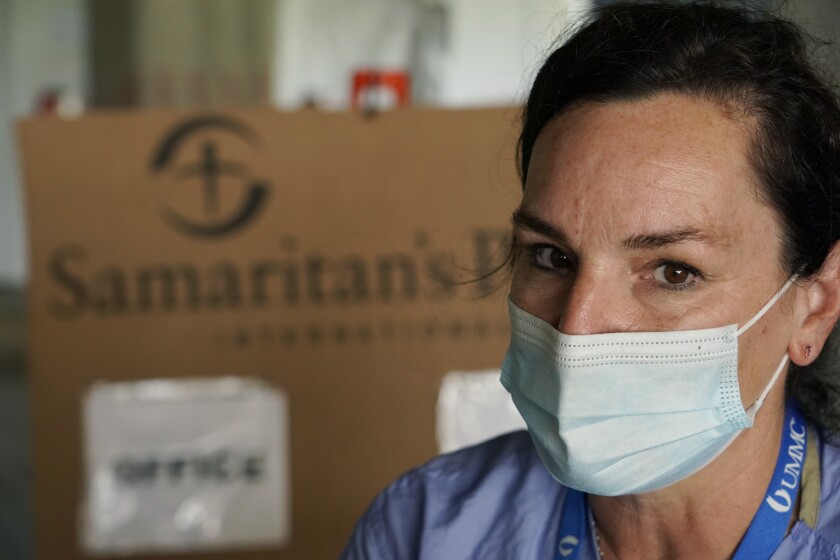 A woman in a mask sits in front of a cardboard box with the words  "Samaritan's Purse.