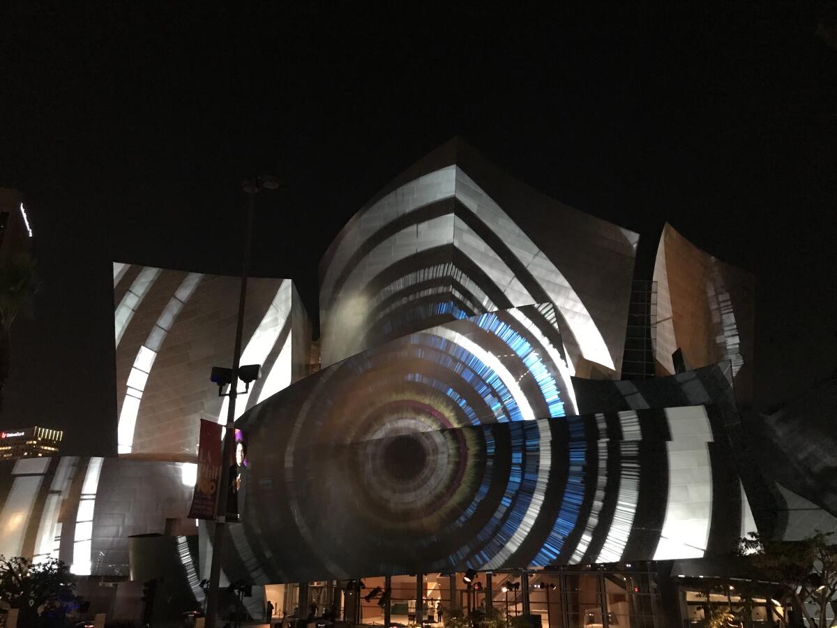 Projections on the side of Disney Hall show blue and white geometric images comes together in the form of an eye.