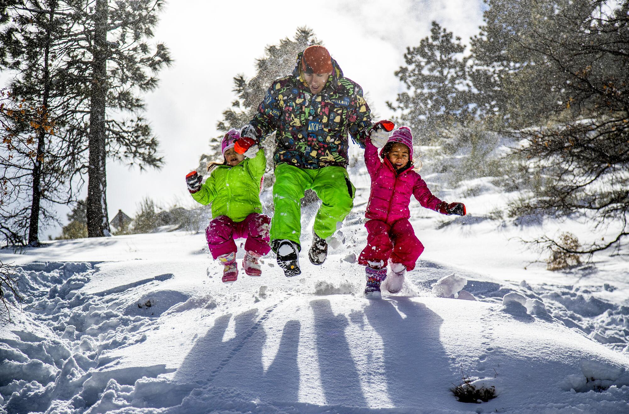 Tomasz Zielinski of Altadena and his daughters  leap into a snow bank