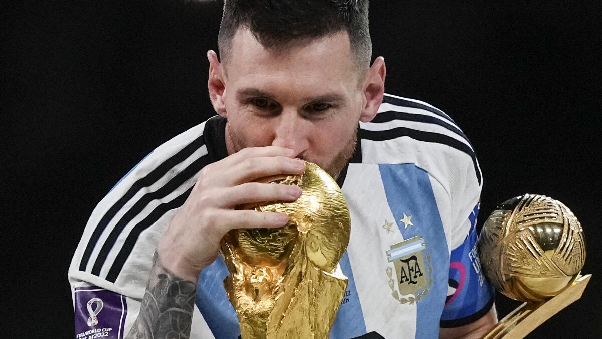 Argentina's Lionel Messi kisses the World Cup trophy with the golden ball trophy in his hand.