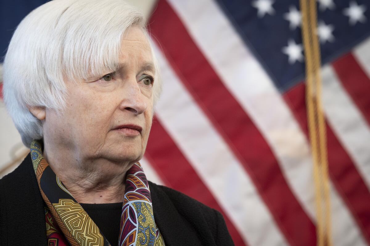 A white-haired woman appears in front of an American flag.