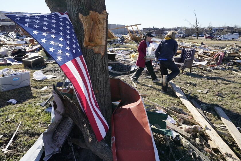 A flag hangs from a tree as two women carry items recovered from tornado wreckage Sunday, Dec. 12, 2021, in Mayfield, Ky. Tornadoes and severe weather caused catastrophic damage across several states Friday, killing multiple people. (AP Photo/Mark Humphrey)