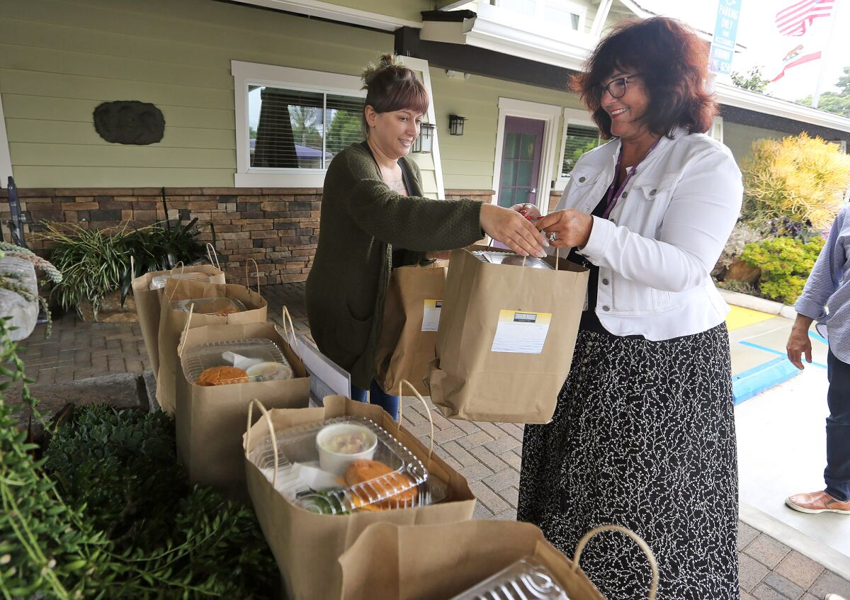 CEO Sue Bright, right, and house chef Fatima Abuzaineh bring in pre-packaged lunches donated by the Tavern House Kitchen + Bar to the New Directions for Women facility in Costa Mesa on Monday.