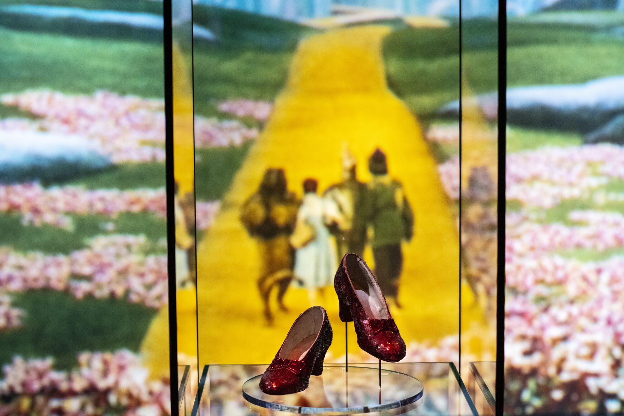 Ruby shoes in a glass case, with a photo of the Yellow Brick Road in the background