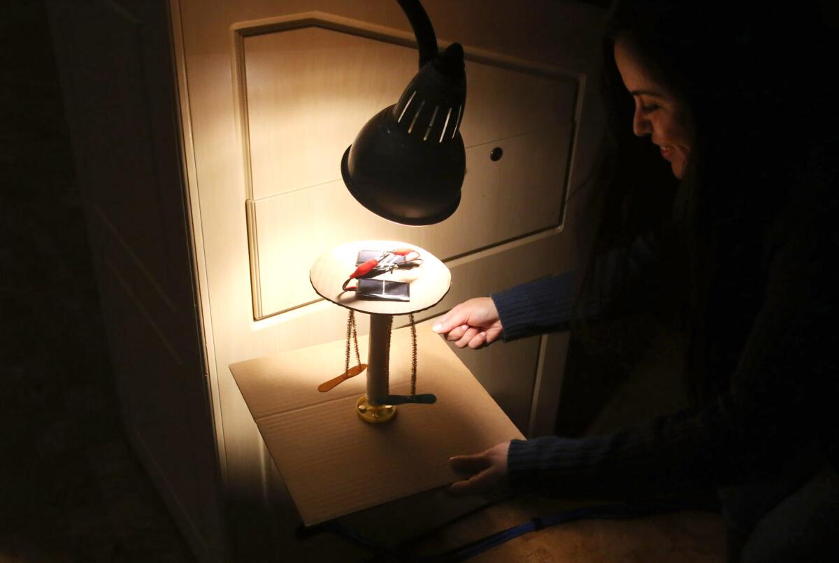 Christine Ramirez, a teacher at Cerritos Elementary School, uses a desk lamp to test her miniature solar carnival ride during workshop at the Glendale Central Library.