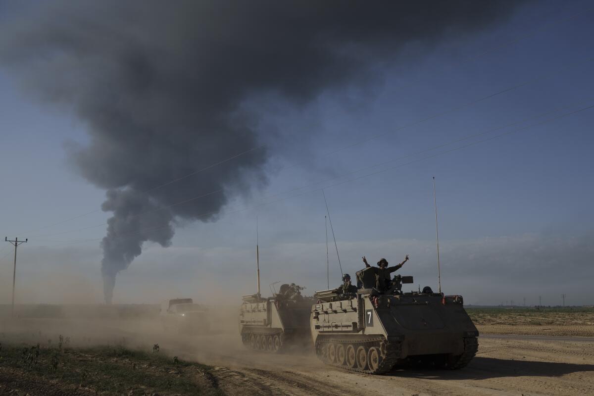 Israeli military personnel carriers near the Gaza border as smoke rises in the distance.