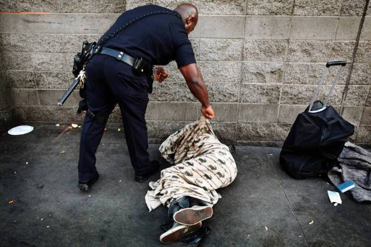 LAPD Officer Deon Joseph tries to wake a man on skid row. Joseph, a nemesis to the beer vendors, says beer and drugs help drive skid row crime.