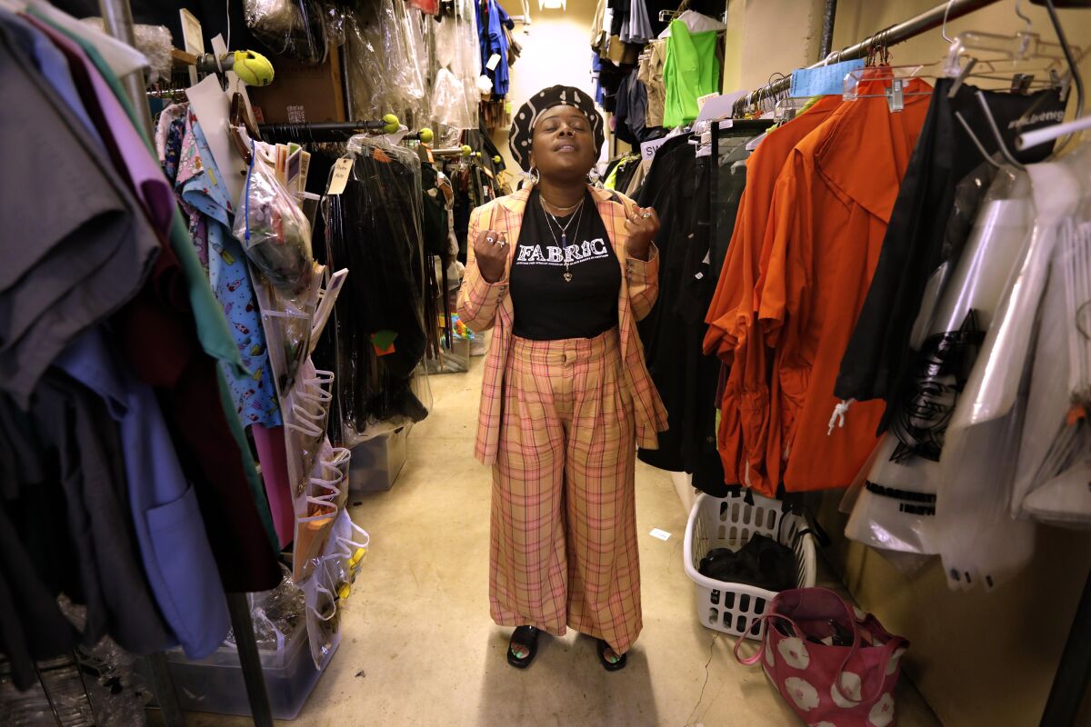 A woman in a colorful pantsuit stands between racks filled with costumes.