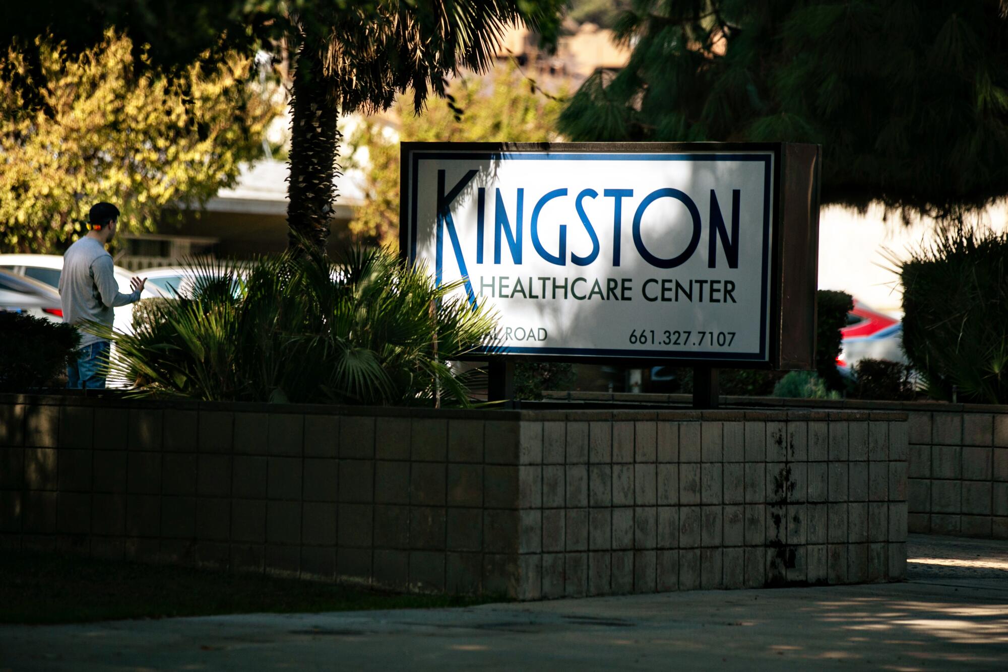 A sign shaded by trees identifies Kingston Healthcare Center