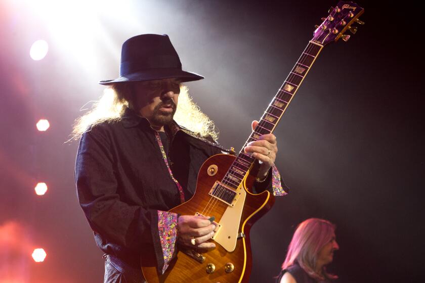 A man with long hair wearing a black fedora and playing the electric guitar on a stage