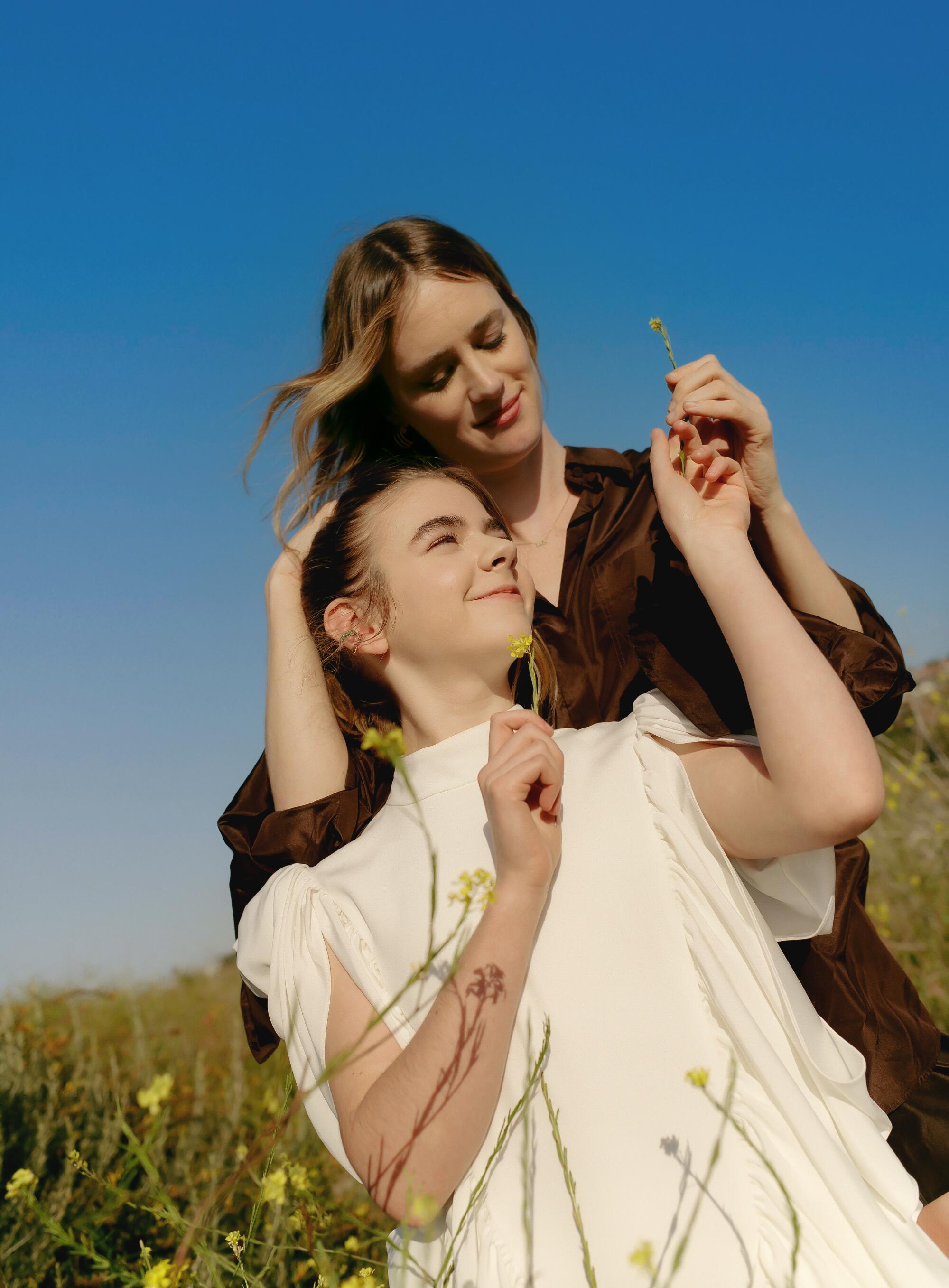 Two women are surrounded by yellow flowers in a field.