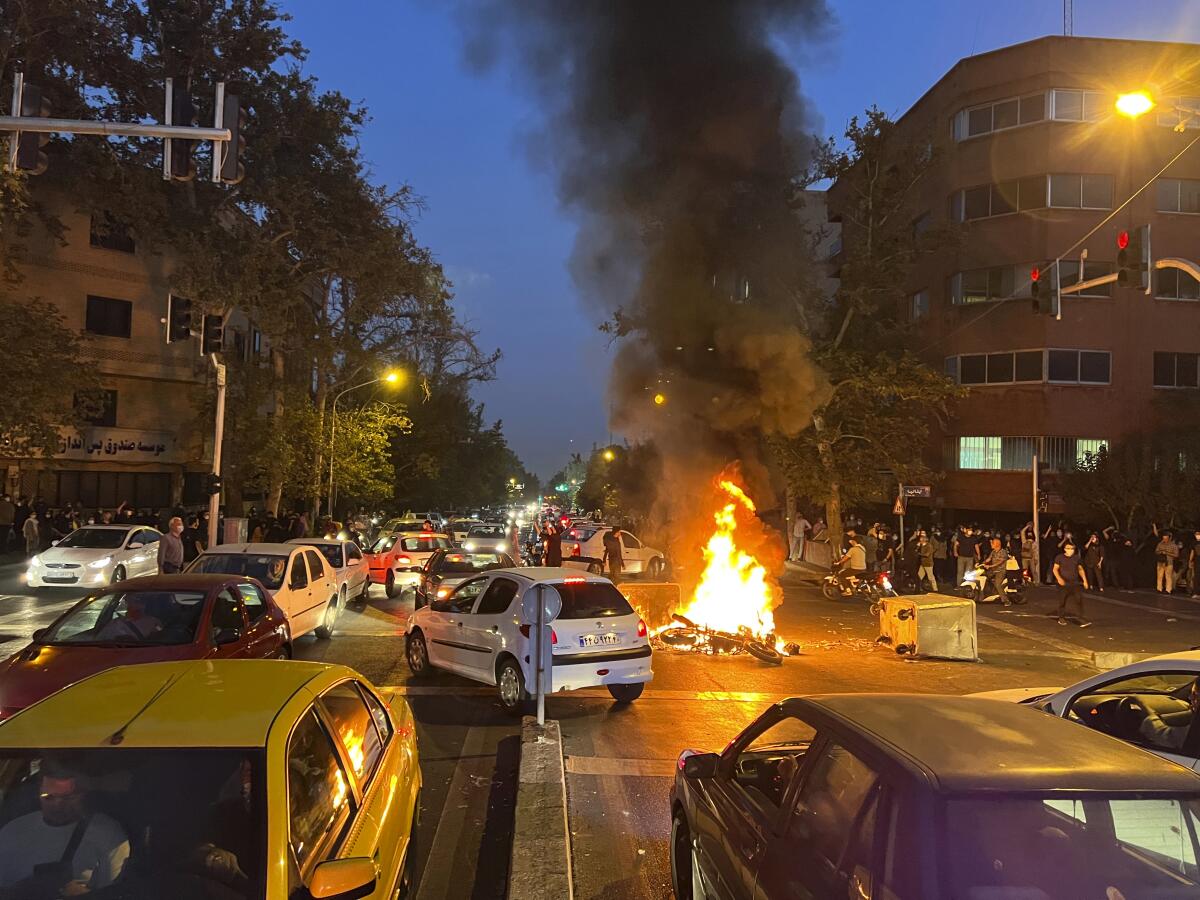 A police motorcycle burns during a protest on a city street in the evening among cars.