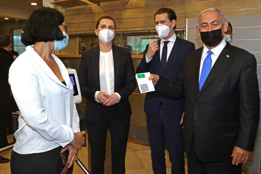 FILE - Then Israeli Prime Minister Benjamin Netanyahu, right, holds a "Green Pass," for citizens vaccinated against COVID-19, as he visits a fitness gym with Austrian Chancellor Sebastian Kurz, second right, and Danish Prime Minister Mette Frederiksen, left, to observe how the pass is used, in Modi'in, Israel, March 4, 2021. Israeli Prime Minister Naftali Bennett said Thursday, Feb. 17, 2022, that the country’s coronavirus vaccination “green pass” system will be suspended as new daily cases of COVID-19 continue to decline. (Avigail Uzi/Pool via AP, File)