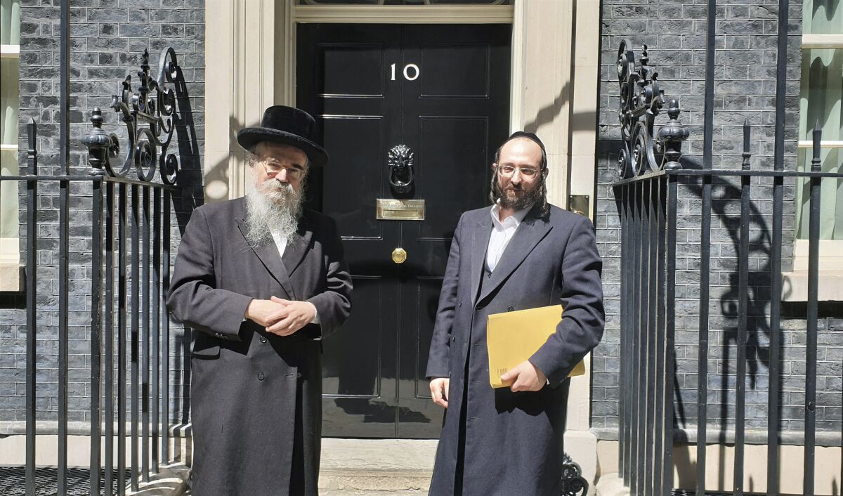 In this photo provided by Chaya Spitz, Rabbi Avrohom Pinter, left, stands beside Joel Friedman, right, the director of Public Affairs for the Interlink Foundation, an umbrella organization for Orthodox Jewish charities on July 4, 2019 in Downing Street, London. Pinter gave his life to save his neighbors. When the British government ordered a lockdown to slow the spread of coronavirus, Pinter went door-to-door to deliver the public health warning to the ultra-Orthodox Jews in northeast London. Within days, the 71-year-old rabbi had caught the disease and died. (Chaya Spitz via AP)