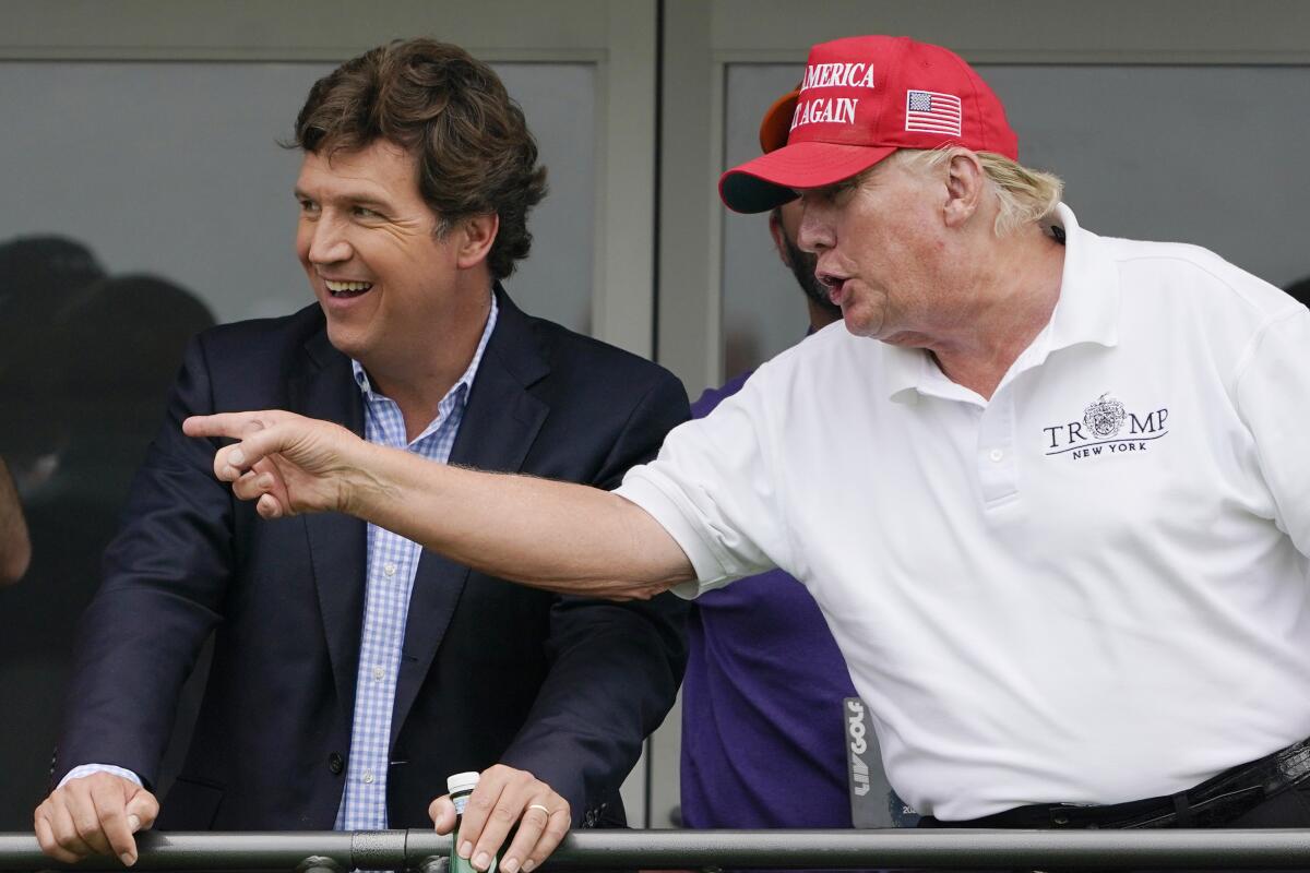 Tucker Carlson, left, and former President Donald Trump, talk while watching golfers 