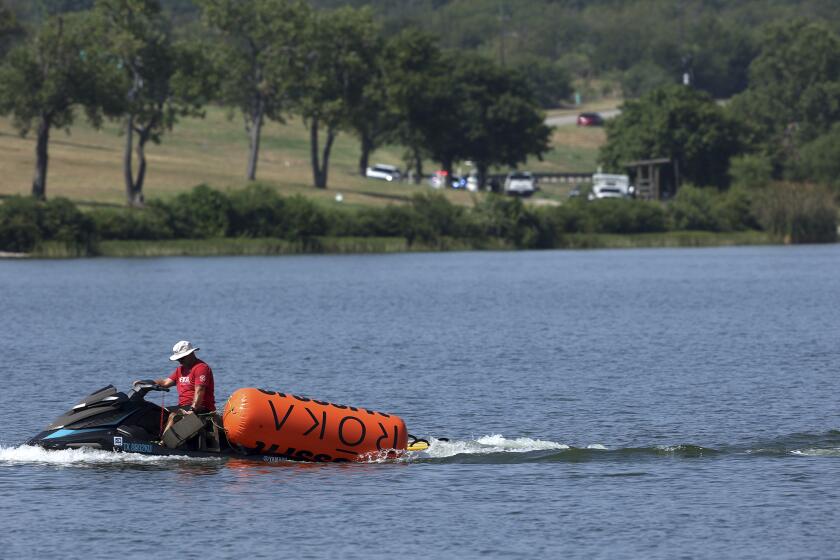 A jet ski pulls in buoys from the CrossFit Games at Marine Creek Lake, where an athlete drowned during the run swim event on Thursday, Aug. 8, 2024 in Fort Worth, Texas, (Amanda McCoy/Star-Telegram via AP)