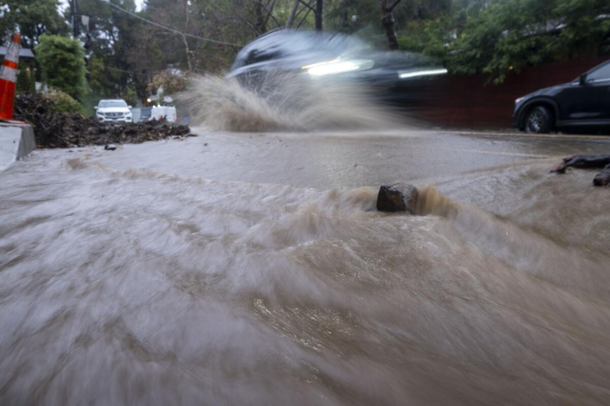 A car drives through a street filled with rainwater near Beverly Glen Boulevard in the Hollywood Hills.