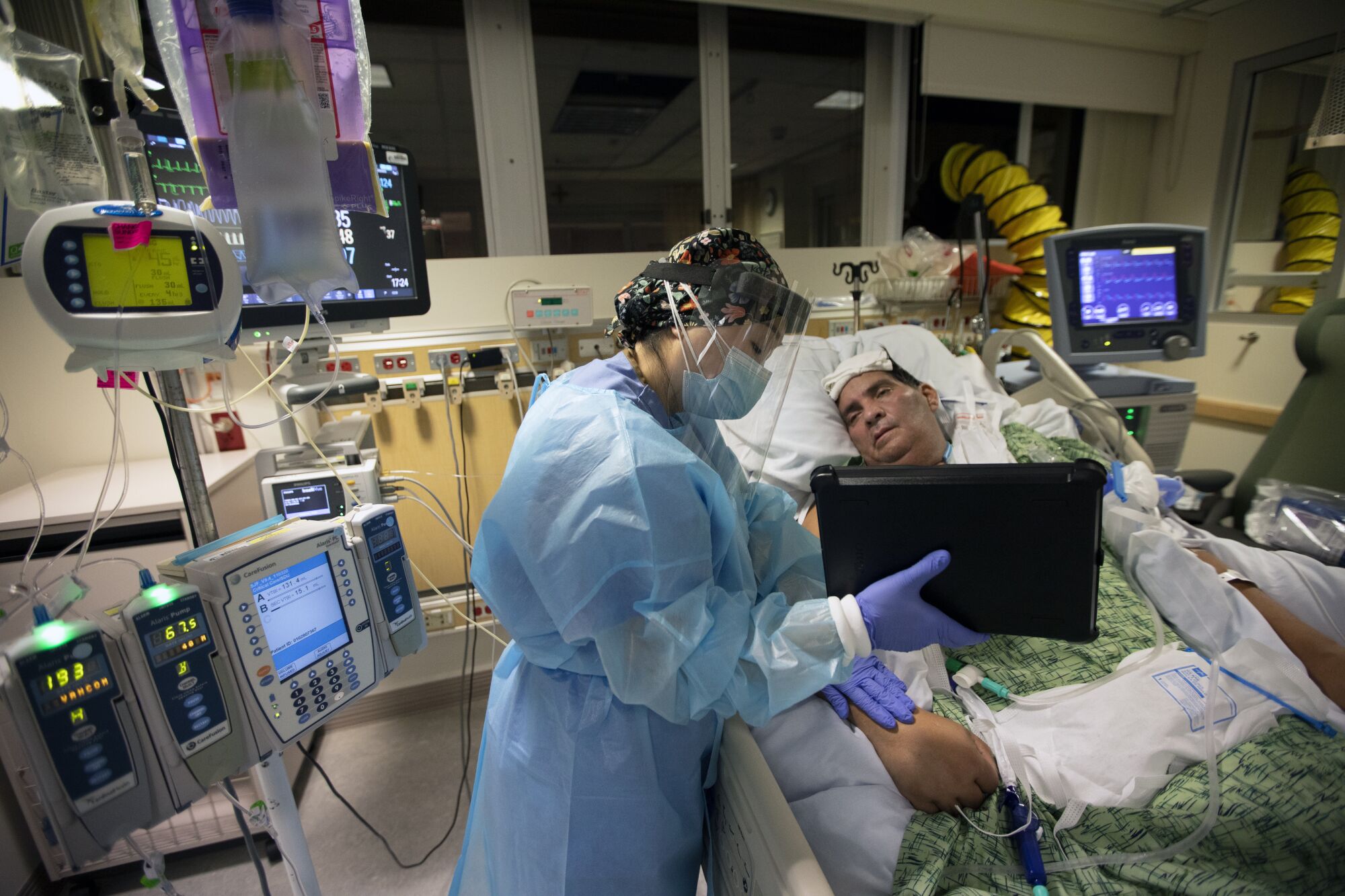 RN Kat Yi holds an iPad up to Eduardo Rojas so that his wife can talk to him.