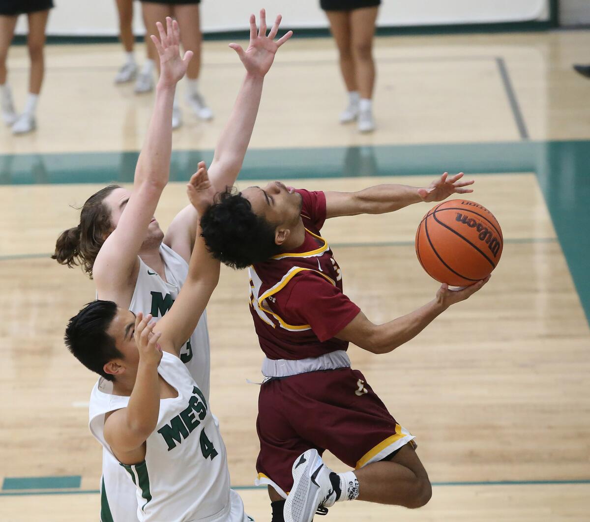Estancia's Marvin Harry drives around Costa Mesa's Christian Dasca (4) and Alec Terry and is fouled during an Orange Coast League game on Wednesday.