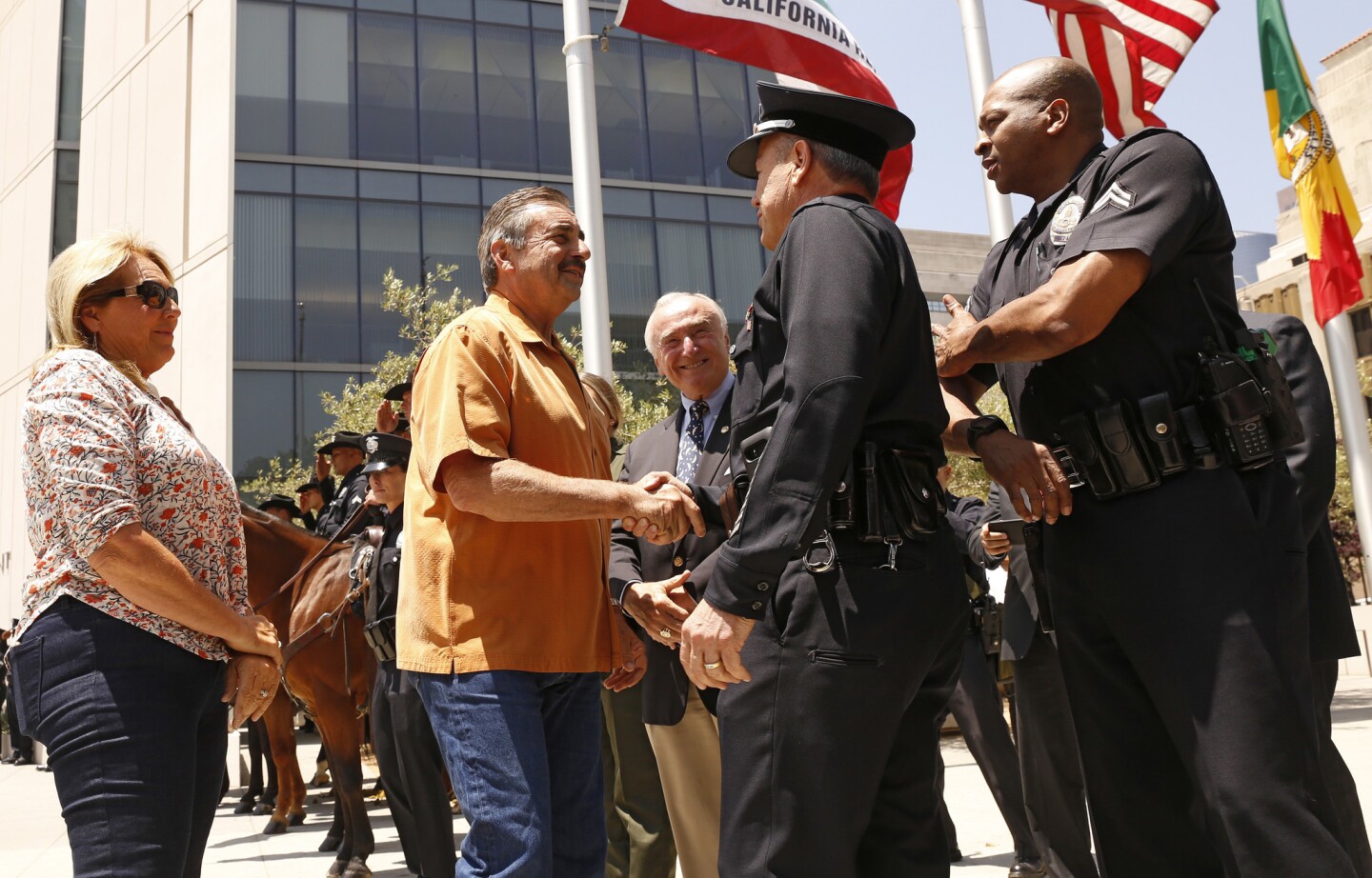 Outgoing LAPD Chief Charlie Beck, second from left, shakes hands with incoming LAPD Chief Michel Moore during a farewell ceremony for Beck outside LAPD headquarters. In center background is former LAPD Chief William Bratton.