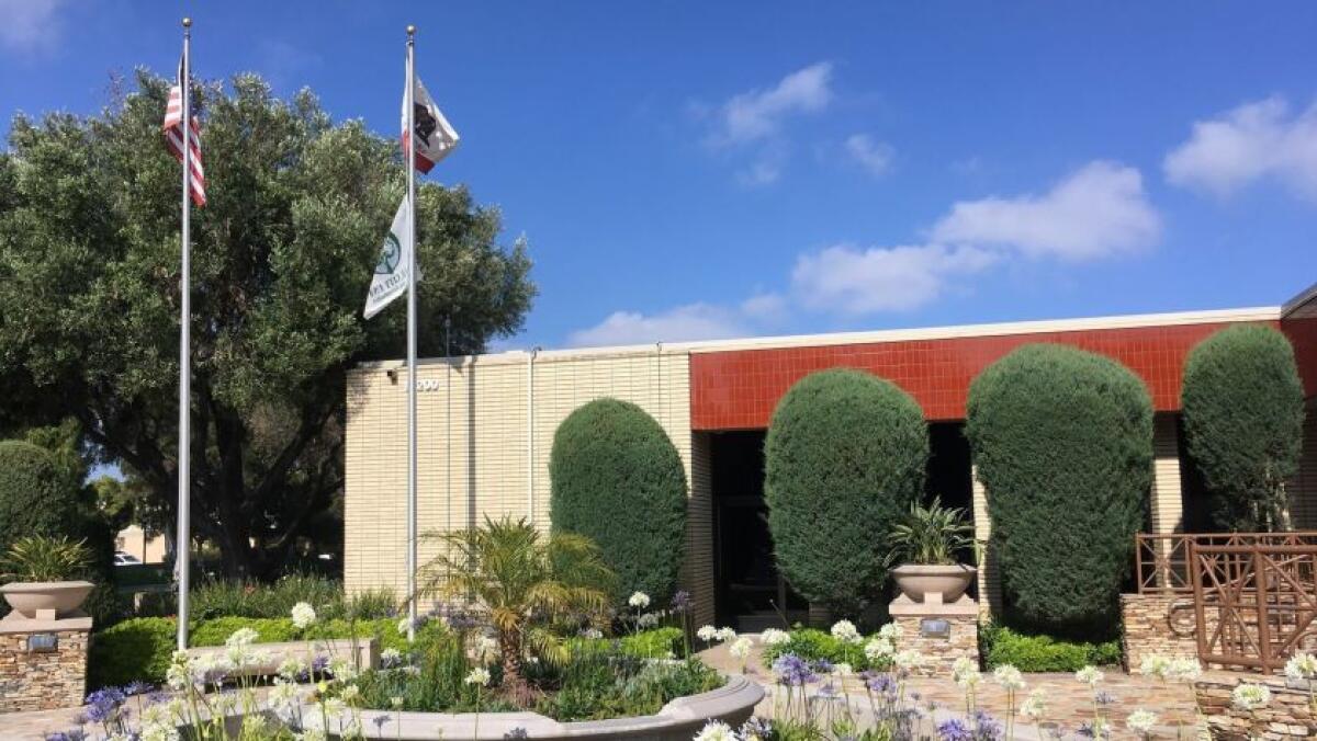 Photo of municipal building blue sky and clouds in background and two flag poles in foreground flying U.S. and California flags and a Tree City USA flag.