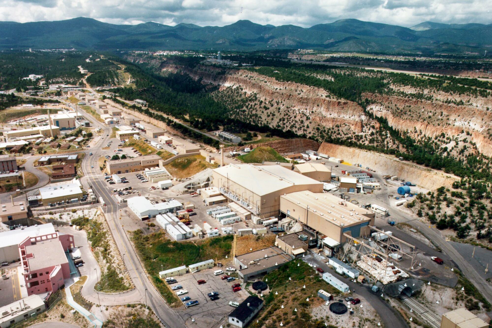 An aerial view of buildings and cars next to forested mountains on the horizon.