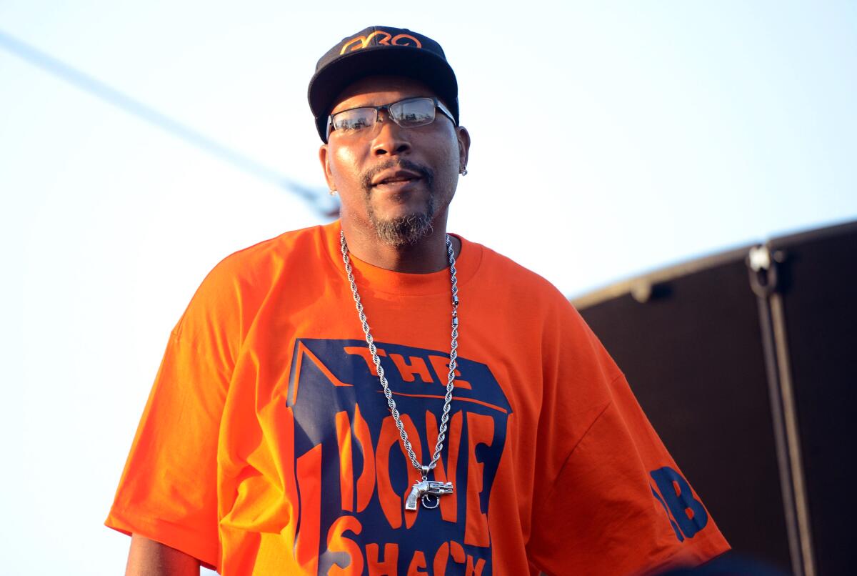  C-Knight wears an orange and blue shirt with a black hat as he performs on an outdoor stage