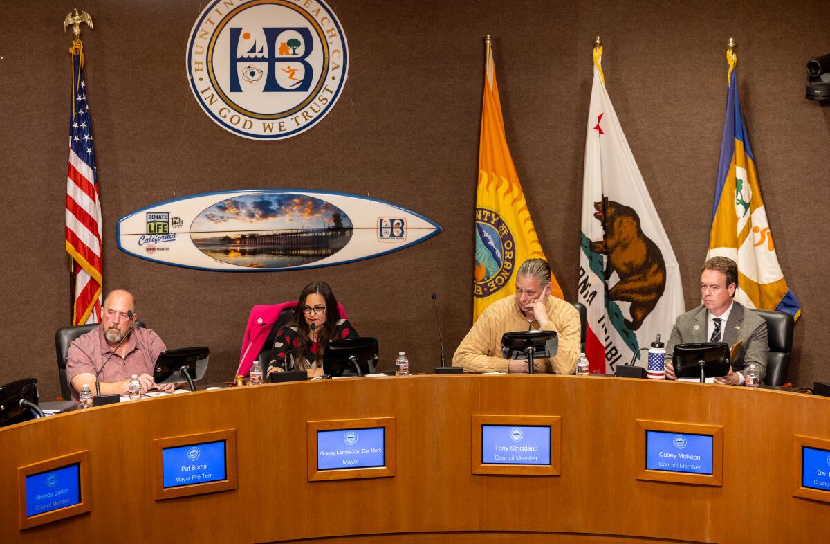  Huntington Beach city council members listen in chambers with flags behind them.