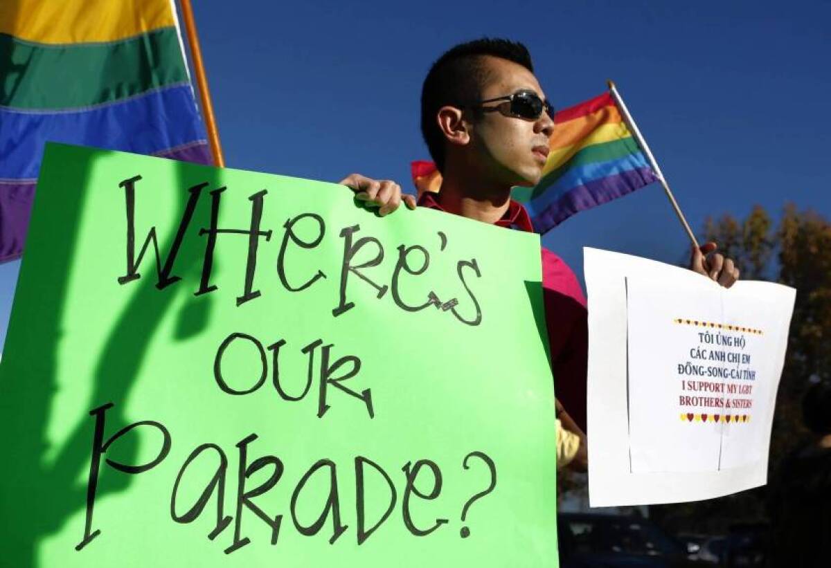 Minh Tran of Westminster holds a sign and LGBTQ Pride flag.