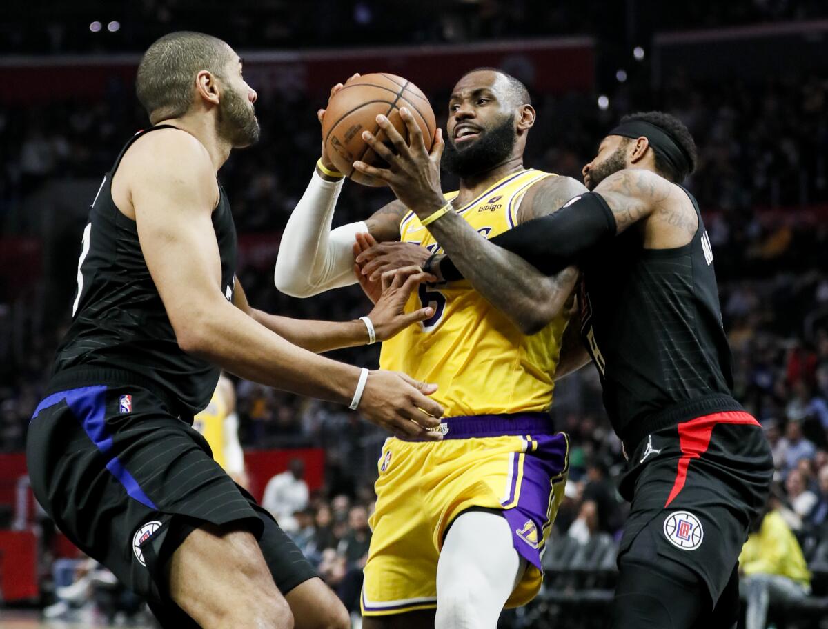 Lakers forward LeBron James is tangled up by Clippers forward Marcus Morris Sr. while driving to the basket.