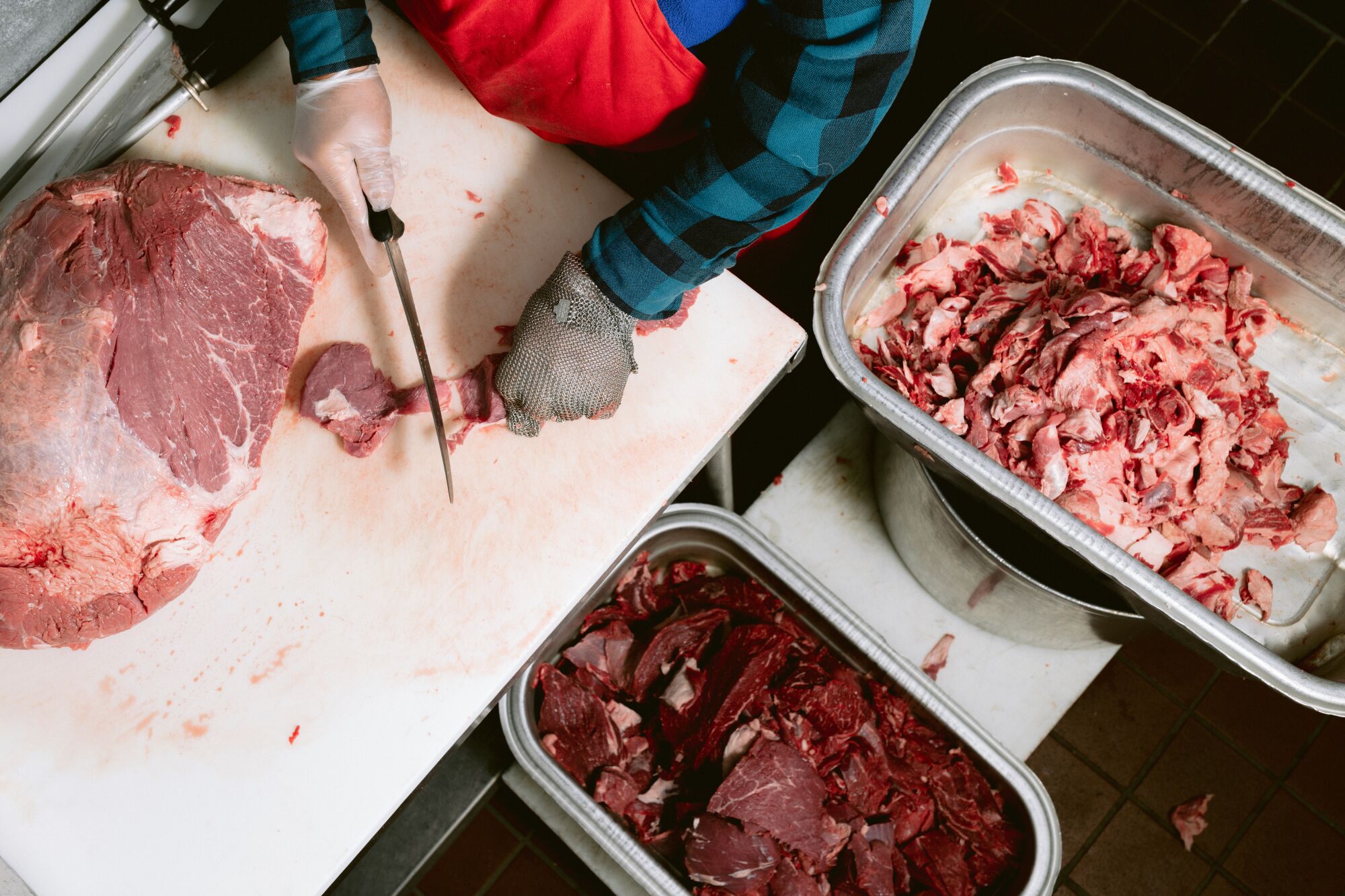 An overhead photo of a man's hands cutting slabs of meat.