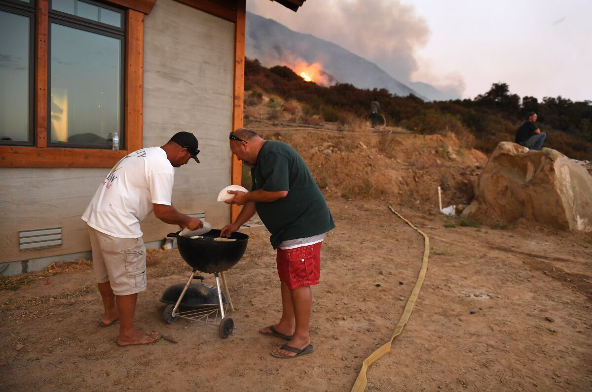 Jeremy Anglin, left, and Matt Taylor heat up tacos on a grill as the El Dorado fire approaches in Yucaipa on Saturday.  