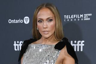 Jennifer Lopez posing in a dress made of mirrored pieces with a capelet over her shoulders