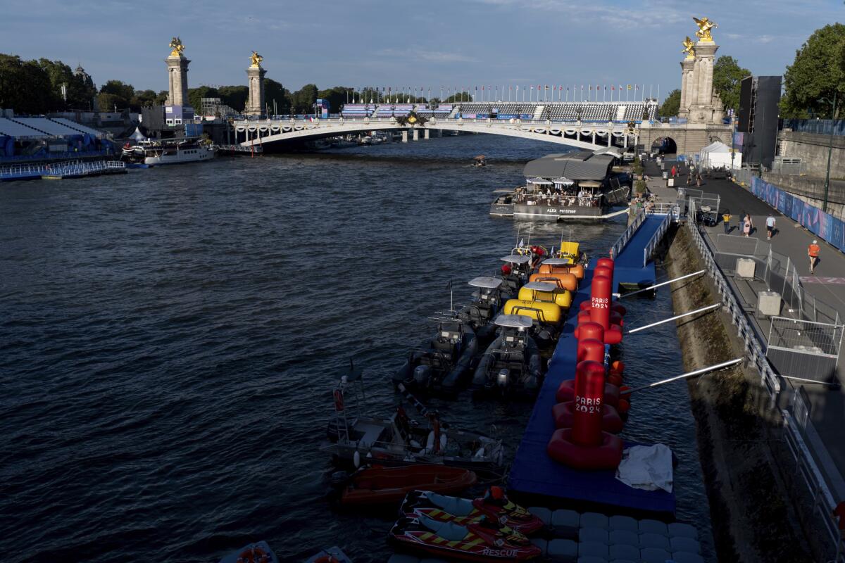 Watercraft and buoys sit along the Seine river as the triathlon event venue looms in the background 