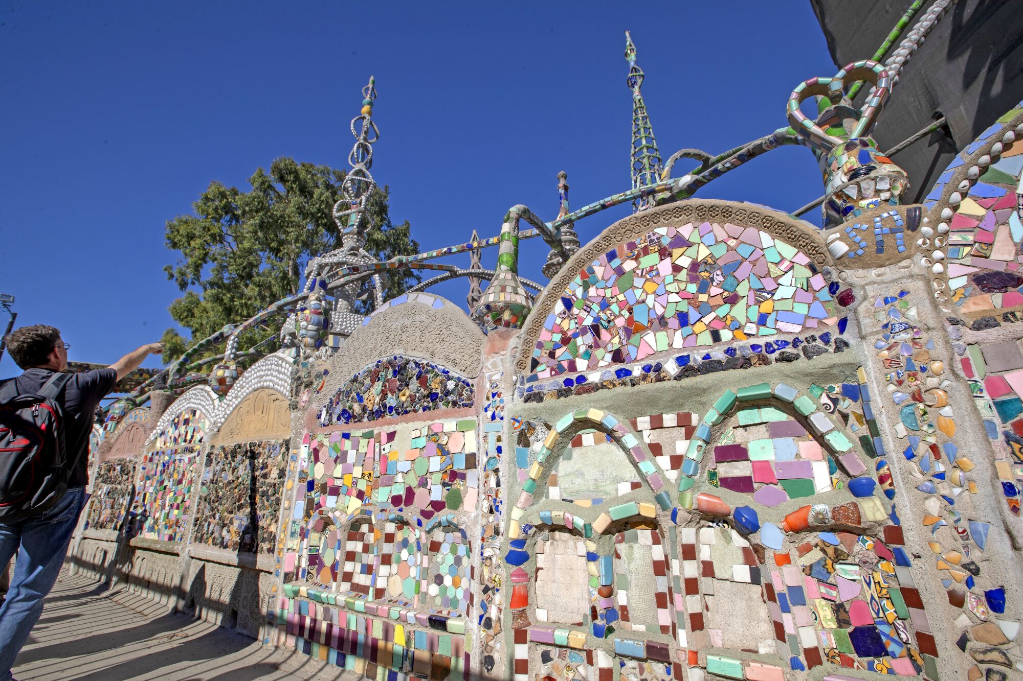 A concrete wall decorated in mosaics, in front of a giant metal tower
